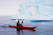 Eco tourist in single sea kayak paddles by an iceberg. Danco Island. Antarctica