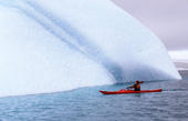 Eco tourist in a sea kayak paddles past an iceberg near Danco Island. Antarctic Peninsula