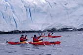 Eco tourists in double kayaks paddle past a glacier near Port Lockroy. Antarctic Peninsula