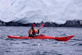Eco tourists in a sea kayak paddles past a glacier near Port Lockroy. Antarctic Peninsula