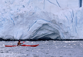 Eco tourist in a sea kayak paddles past a glacier near Port Lockroy. Antarctic Peninsula
