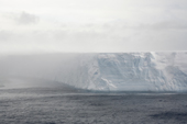 The lee side of a large tabular iceberg is almost hidden by the snow blowing off the top of it in windy weather. Antarctica