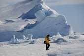 Yellow jacketed tourist takes a quiet moment by a grounded iceberg. Snow Hill Island. Antarctica.