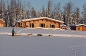 Musher & dog sled take a trail in front of a log cabin. North Pole. Alaska. 1989