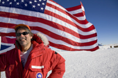 Philip Laura, a baker at South Pole Station at the Ceremonial South Pole with the Stars & Stripes. Antarctica.