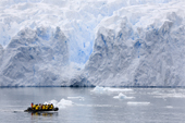 Zodiac full of passengers cruises in front of a glacier in Cierva Cove, an inlet in mainland Antarctic Peninsula