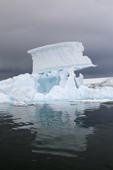 Sculptural iceberg with a large chunk of ice balanced on high against dark water skies. Fish Islands. Antarctica