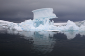 Sculptural iceberg with a large chunk of ice balanced on high against dark water skies. Fish Islands. Antarctica
