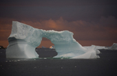 Iceberg with an ice arch grounded in Marguerite Bay. Sunset colours the clouds and the sea Antarctica