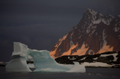 Iceberg with an ice arch grounded in Marguerite Bay. Sunset colours the snow slopes. Antarctica