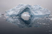 Iceberg with an ice arch and reflections on a snowy day. Whittle Peninsula. Antarctica