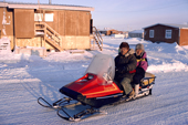 Warmly dressed Inuit couple ride to shops on their snowmobile. Igloolik, Canada. 1995