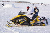 Bernadette Arnatsiaq, an Inuit woman, drives her snowmobile wearing a traditional Baffin Island parka with her son on the back. Igloolik, Nunavut, Canada. 2008