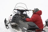 Using his snowmobile to lean on, Inuit hunter Noah Metuq, sights his rifle before a seal hunt in Cumberland Sound. Pangnirtung, Nunavut, Canada. 2008