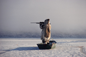 Inuk stands in floe edge boat at the ice edge, & aims his rifle, while hunting. Igloolik, Nunavut, Canada. 1990