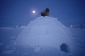 At dusk, an Inuit hunter, puts the finishing touches to an Igloo he has built. Igloolik, Nunavut, Canada. 1990