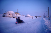 Inuk on a snow mobile passes the geodetic houses in Baker Lake at dusk. Nunavut. Canadian Arctic. 1982