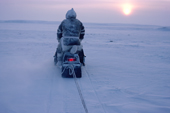 Inuit hunter, Tom Kudloo on a hunting trip on his snowmobile at sunset. Baker Lake. Nunavut. Canadian Arctic. 1982