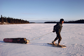 Billy Edwards, an elderly Cree in snowshoes, hauling a birchwood sled over lake ice. Quebec, Canada. 1988