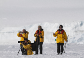 Tourists with cameras and walking poles visit the Emperor Penguin colony at Cape Washington. Antarctica