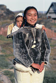 Eqilana Simigaq, an Inuit woman, carries her son Peter in a sealskin Amaut (traditional hooded jacket) at Qeqertat. Inglefield Bredening. Northwest Greenland. (1980)