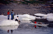 Inuit hunter, Preben Petersen, holds the bow of his kayak as his son plays in it. Qeqertat, Northwest Greenland. 1980