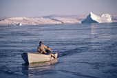 Jens, an Inuit hunter, returns to the village of Moriussaq with a seal over the side of his boat after an autumn day's hunting. Moriussaq. Northwest Greenland. (1987)