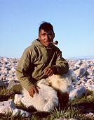 Angutikavasaq Duneq, an Inuit man, smoking his pipe at a summer hunting camp in Inglefield Bay. He is wearing a traditional anorak and Polar Bear skin trousers. Qaanaaq, Avanersuaq, Northwest Greenland. (1971)