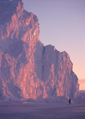 Light from the setting sun reflects off the surface of a big iceberg, note small figure. N.W.Greenland. 1998