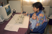 Sofie Jensen, an Inuit girl, holds a friend's baby while using a computer at her home in Qaanaaq. Northwest Greenland. 1998