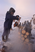 Yakut man using a chain saw to cut firewood during the winter in Verkhoyansk. Yakutia, Republic of Sakha, Russia. (1999)