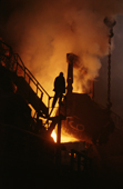 A worker is silhouetted by red hot metal at the copper foundry in Norilsk. Western Siberia, Russia. 2000