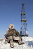 Jakov Vanuito, a Nenets reindeer herder, sits infront of a gas drilling derrick near Tambey in the South Tambey gas field. Yamal Peninsula, Western Siberia, Russia