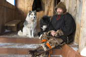 Yemilian Kutyamov, a Khanty reindeer herder,together with his dogs. He is dressed in traditional reindeer skin clothing, outside his home in Ovgort. Shuryshkarsky Region, Yamal, NW Siberia, Russia