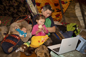 Two year old Daria Serotetto, a Nenets girl, watches children's cartoons on a Laptop with her father, Leova, inside the family's reindeer skin tent. Yamal. NW Siberia, Russia