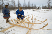 Sergey Serotetto, a Nenets reindeer herder, making a traditional sled from larch wood, while his son Leova watches. Yamal, NW Siberia, Russia