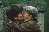 Mandy and Max kiss by the river, love with a tweed cap. Scotland