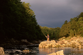 Edward fishing from the big rock, with thundery skies behind him. River Findhorn. Scotland.