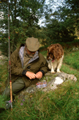 Bryan ties a salmon fly onto his line, watched by Springer Spaniel Puffin. River Findhorn. Scotland.