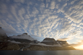 Altocumulus and stratus clouds low around the mountains in Scoresbysund Fiord. East Greenland.